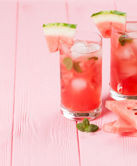Two glasses of watermelon ice tea garnished with watermelon and mint leaves