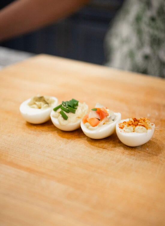 Deviled eggs on a wooden chop block with variations in garnishes