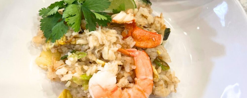 Crab fried rice with pineapple garnished with lime, cilantro, and shrimp.